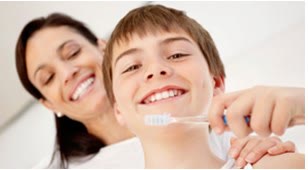 Adolescent care se spală pe dinți, cu mama alături, zâmbind
