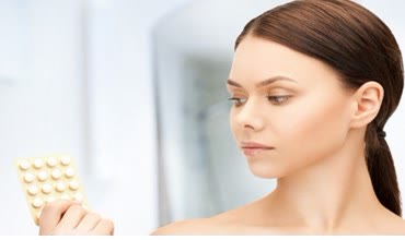Femeie care privește un blister de contraceptive orale