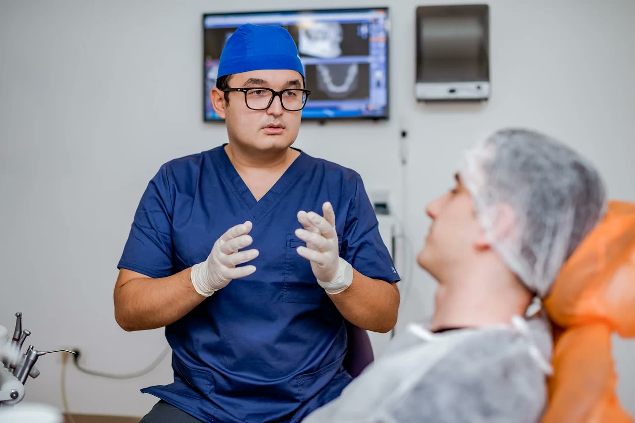 Medic Implantodent explicând pacientei planul de tratament parodontal, cu imaginile tomografiei dentare afișate pe monitorul din cabinet