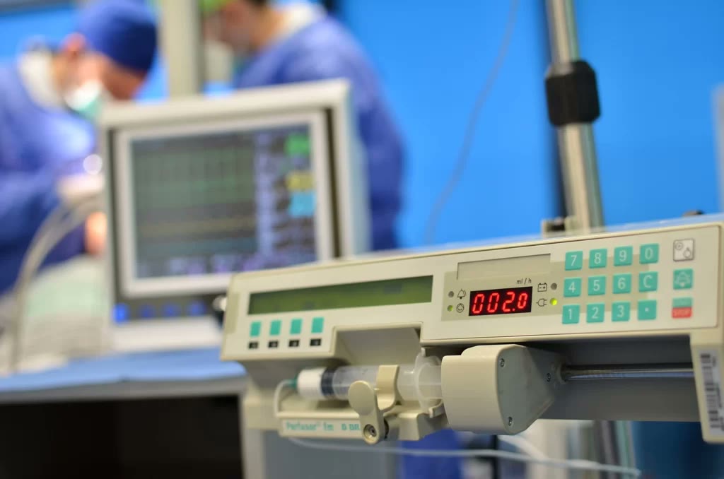 Injectomat și monitor de funcții vitale în blocul operator, cu echipa medicală lucrând în plan secund
