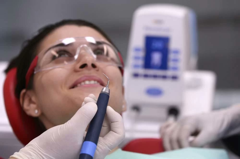 Pacientă în scaunul stomatologic, cu ochelari de protecție, în timpul unei igienizări profesionale cu ansă de ultrasunete piezoelectrice