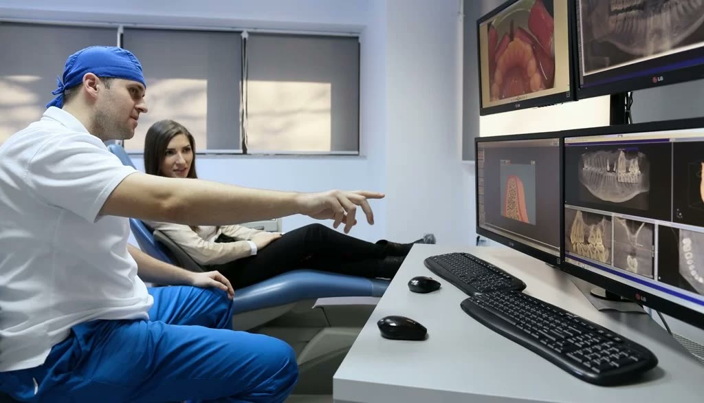 Medic Implantodent arată pacientei imaginile tomografiei 3D pe monitoarele din cabinetul de consultație