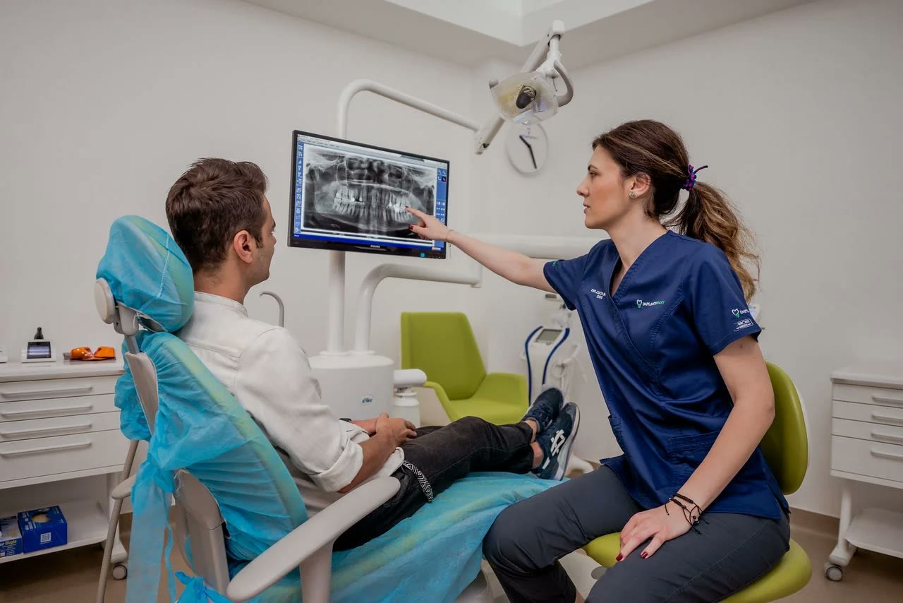Medic Implantodent explicând pacientului radiografia panoramică afișată pe monitorul din cabinet