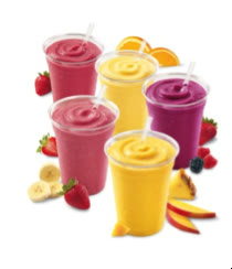 Mai multe pahare cu smoothies din fructe, alături de căpșuni, banană, mango și portocală